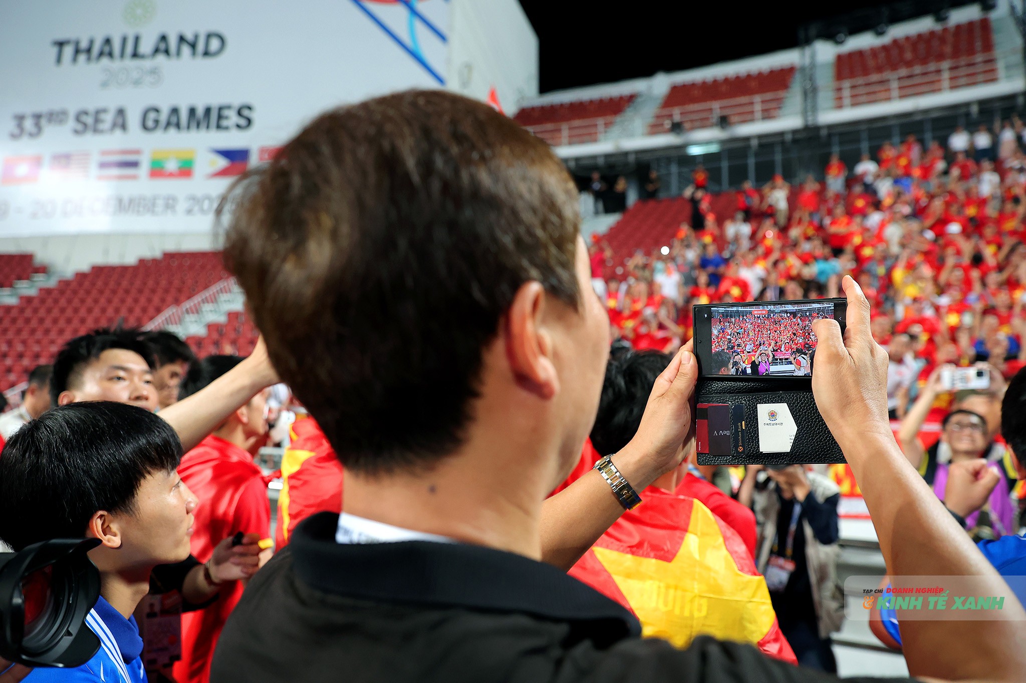 HLV Kim Sang Sik dùng điện thoại lưu lại khoảnh khắc ăn mừng của cổ động viên Việt Nam trên sân vận động Rajamangala